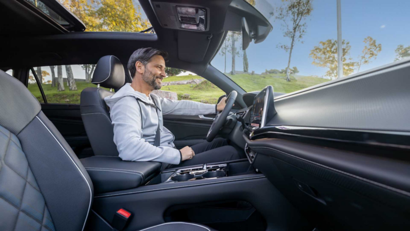 Conductor dentro de una camioneta de lujo Volkswagen toma el volante mientras sonríe. 