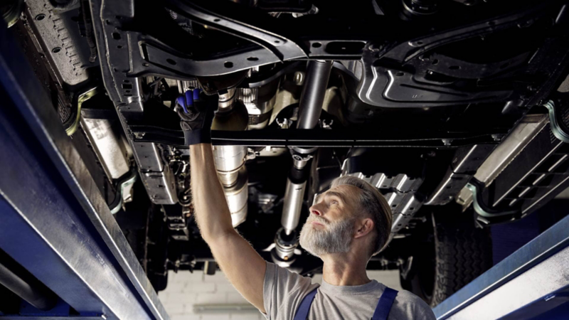 Técnico especializado revisa el sistema de suspensión y escape de un Volkswagen desde abajo. Servicio de mantenimiento VW