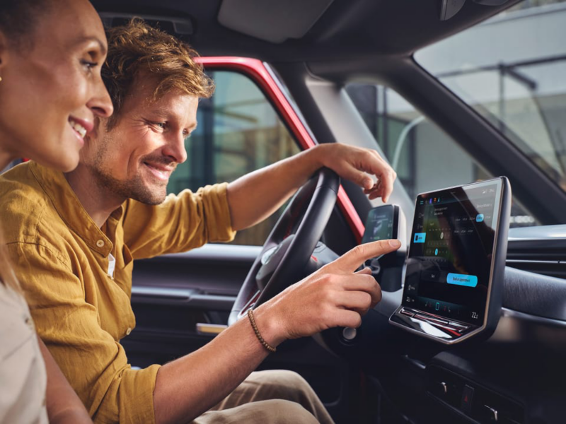 Dos personas sentadas en un vehículo VW, usando la pantalla del salpicadero.