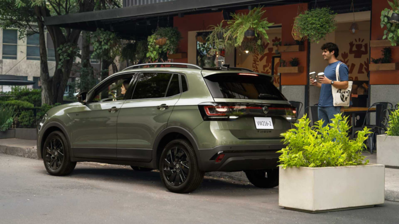 Volkswagen Taigun verde oliva estacionado frente a una cafetería con personas y plantas.