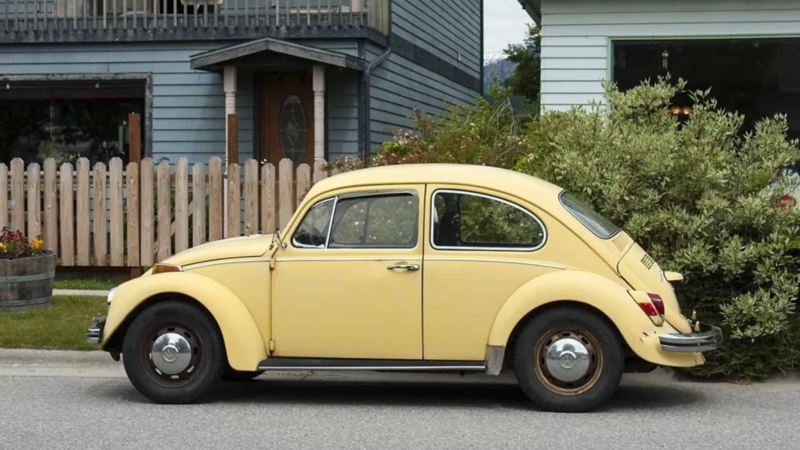 Vocho amarillo, auto clásico de Volkswagen a las afueras de una casa de los suburbios. 