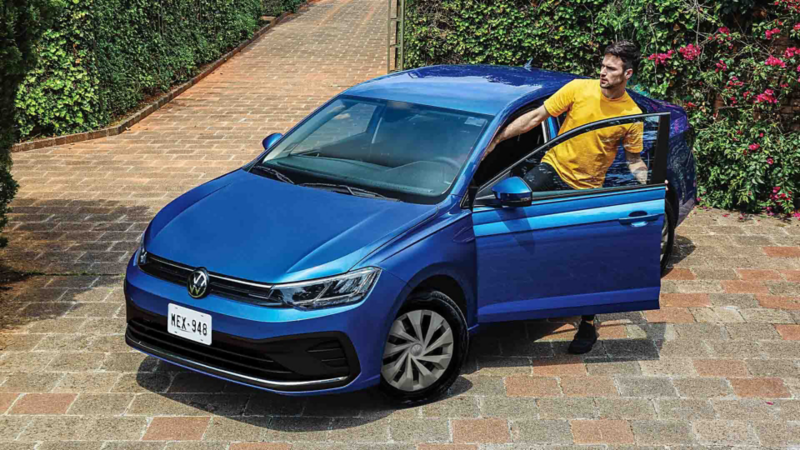Conductor con playera amarilla aborda Volkswagen Virtus 2024, auto sedán de color azul. 
