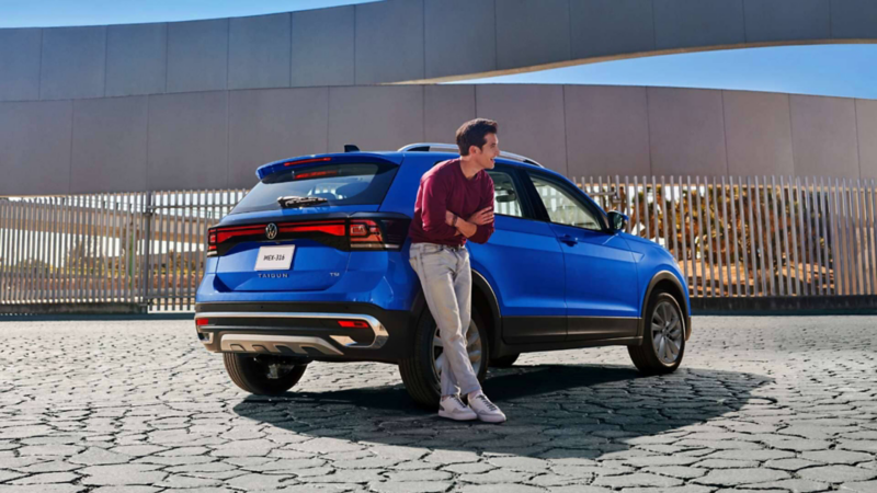 Nuevo Taigun 2023 en color azul, con joven conductor recargado sobre SUV. 