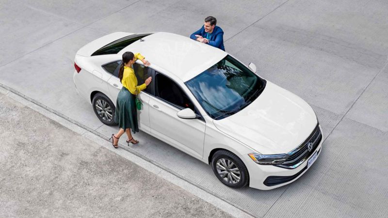 Jetta 2023, sedán en color blanco con pareja que platica alrededor de auto. 