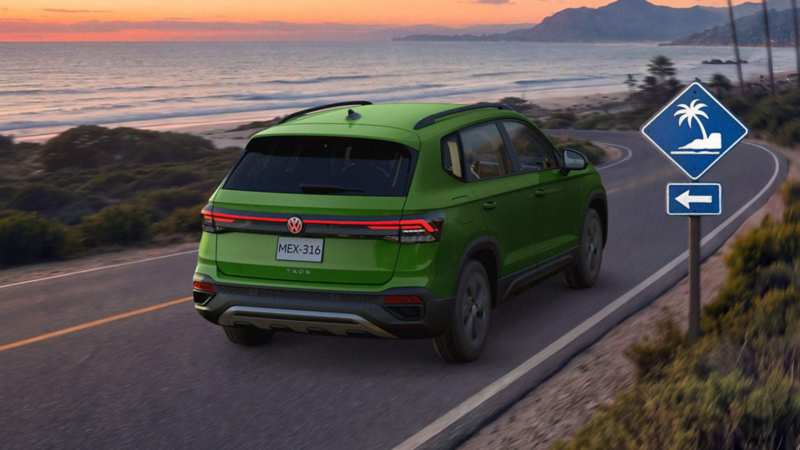 VW Taos. Vista trasera de SUV de color verde en carretera costera, con señalamientos de playa cercana. 