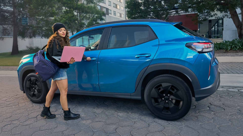 Mujer con computadora portátil en mano sube a Volkswagen Tera 2026 de color azul. 