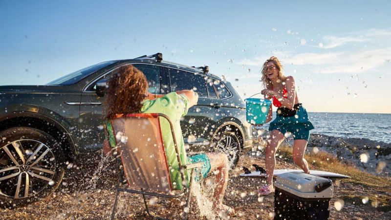 Vista di due ragazze sorridenti mentre scherzano e si divertono in spiaggia e accanto a loro parcheggiato un veicolo Volkswagen.