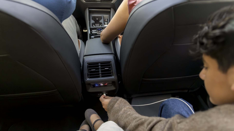 Niño conecta cable a entrada tipo C para cargar dispositivo móvil en Tiguan 2025. 