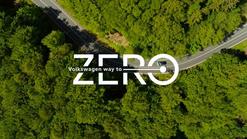 Schriftzug Volkswagen Way to Zero vor Luftaufnahme eines Waldes