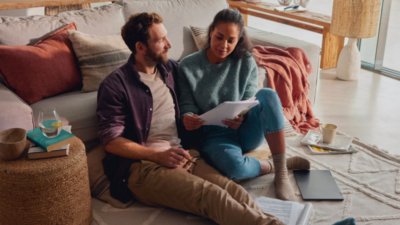 Un couple assis dans son salon, inspecte des documents de financement.