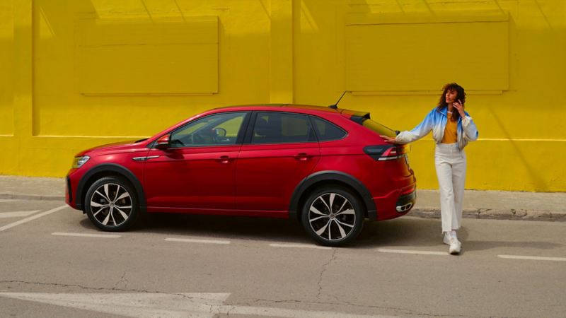 Volkswagen Nouveau Taigo rouge garé dans une rue devant un immeuble jaune avec une femme à l'arrière