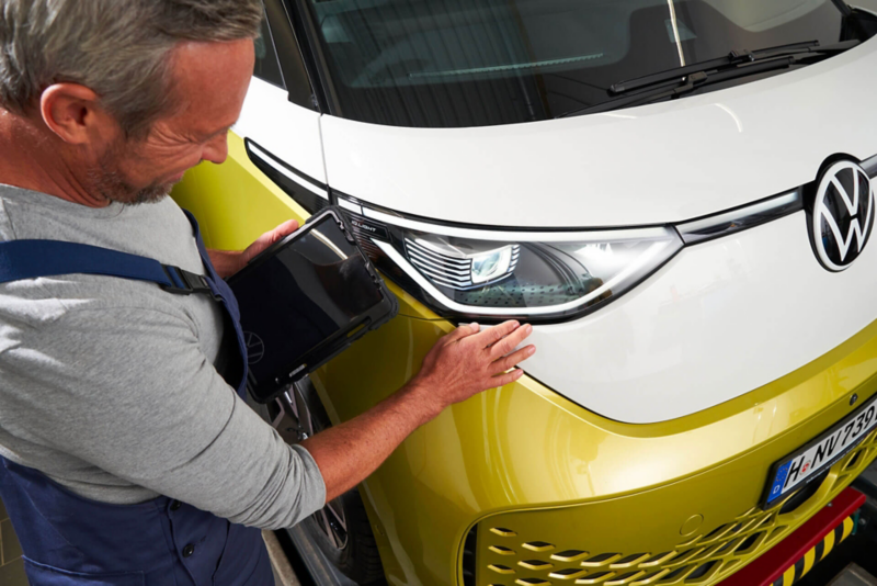 Un technicien Volkswagen inspecte le phare avant d'un ID. Buzz, tablette à la main.