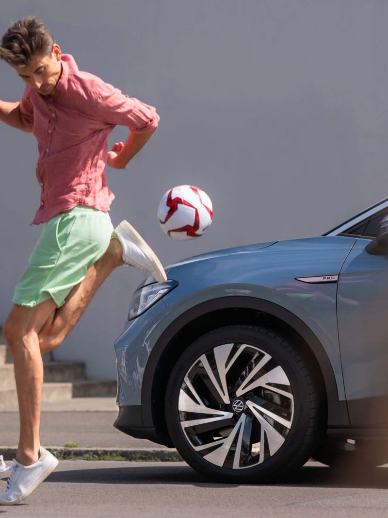 Un homme jongle avec un ballon devant une VW ID.4.