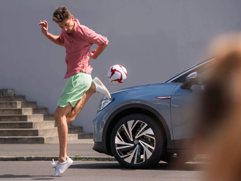 Un homme jongle avec un ballon devant une VW ID.4.