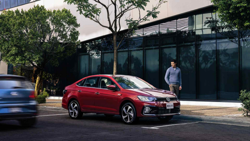 Hombre con suéter azul mira un auto sedán de Volkswagen en color exterior rojo. 