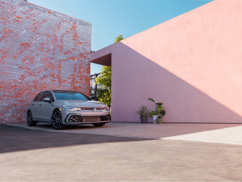 Vista frontal de ¾ de un VW GTI gris estacionado frente a una pared de ladrillos desgastada.