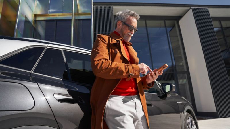 Un homme consulte son smartphone, adossé à sa Volkswagen ID.