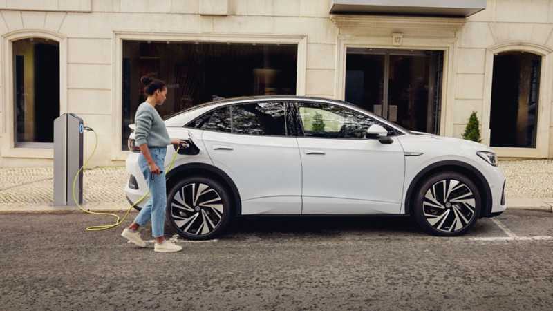 Une femme recharge son Volkswagen ID.5 blanc sur une borne dans la rue.