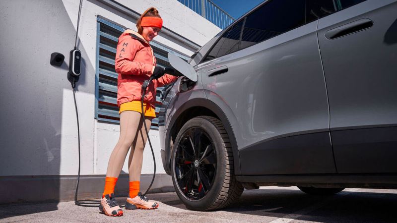 Une femme branche sa Volkswagen ID. sur une borne de voyage.