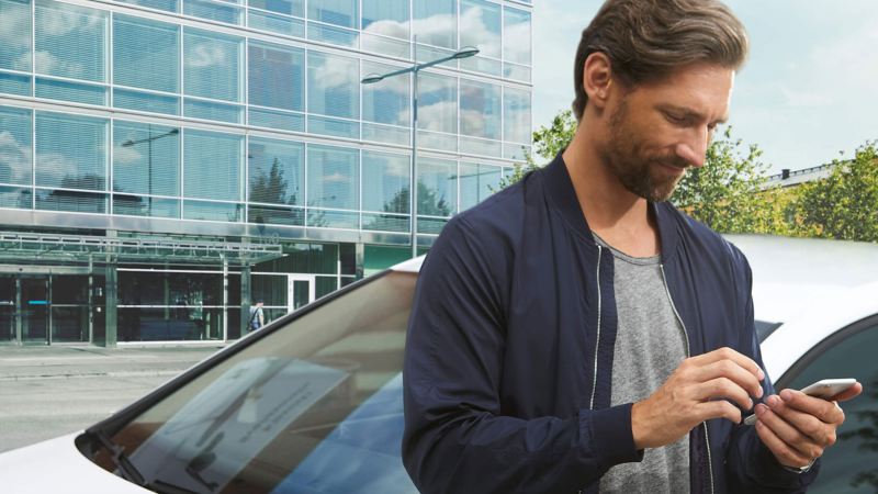 A man standing beside his car checking his mobile app
