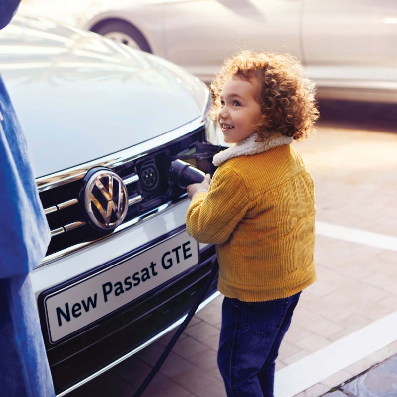 A young child connecting a plug to the front of a Volkswagen Passat GTE