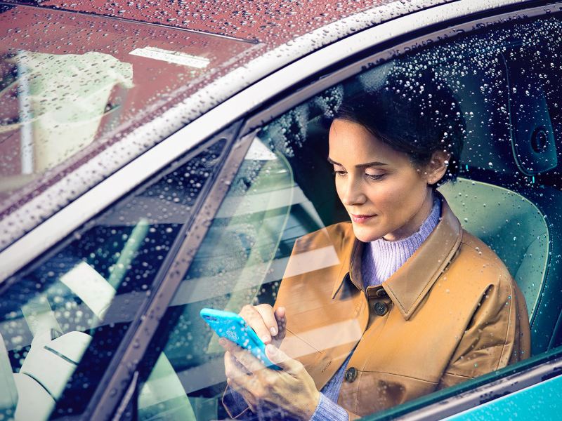 Une femme dans sa Volkswagen ID.3 consulte son téléphone assise côté conducteur avec la fenêtre fermée.