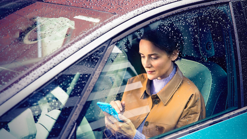 Une femme dans sa Volkswagen ID.3 consulte son téléphone assise côté conducteur avec la fenêtre fermée.