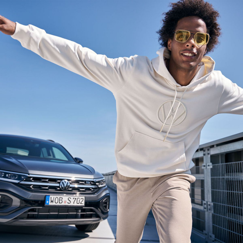 Hombre con prendas de Volkswagen Essentials junto a un automóvil Volkswagen.
