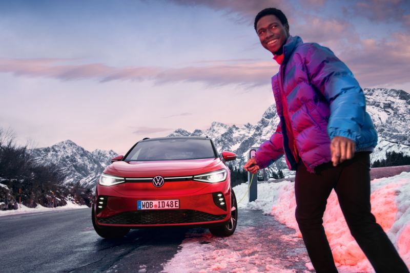 Zu sehen ist ein roter VW ID.4 GTX in verschneiter Landschaft. Davor ein Mann mit blauer Winterjacke. 