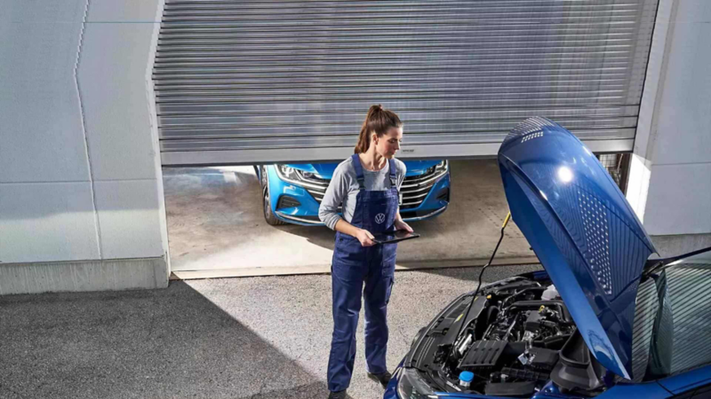 Técnica de Volkswagen checa motor en el cofre abierto de un SUVW, dentro de taller de reparación. 