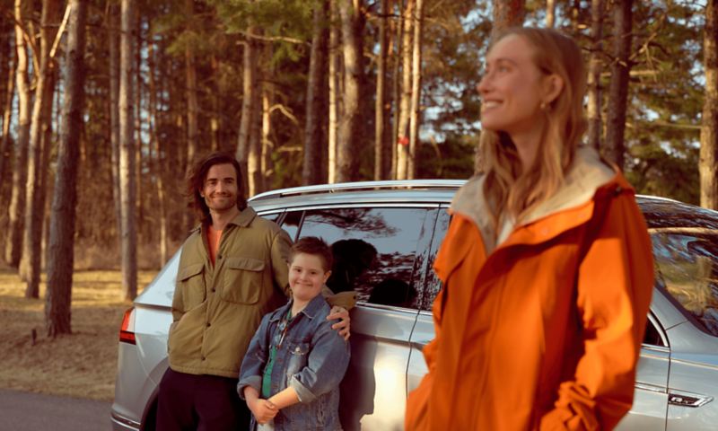 A happy family standing next to a Pyrite Silver Metallic 2022 Tiguan in a forest.