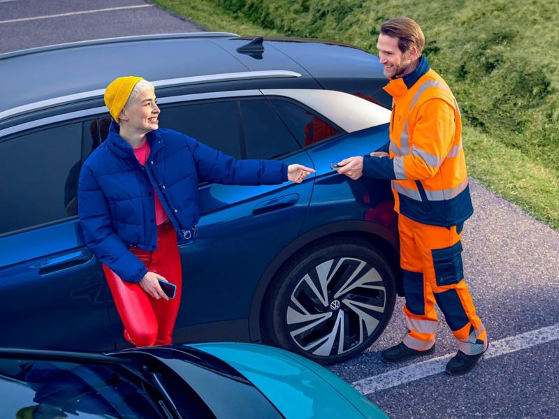 Zijaanzicht van een blauwe VW ID.4, twee mensen praten met elkaar, op de voorgrond de achterkant van een VW ID.3