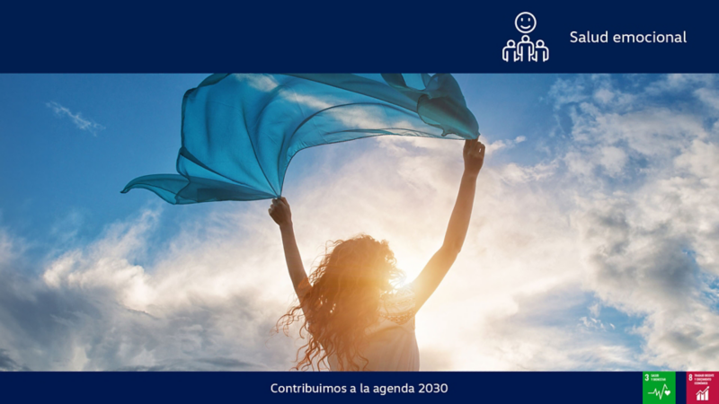 Mujer sujeta una tela transparente que mueve el viento en un paisaje con cielo azul y nubes. 