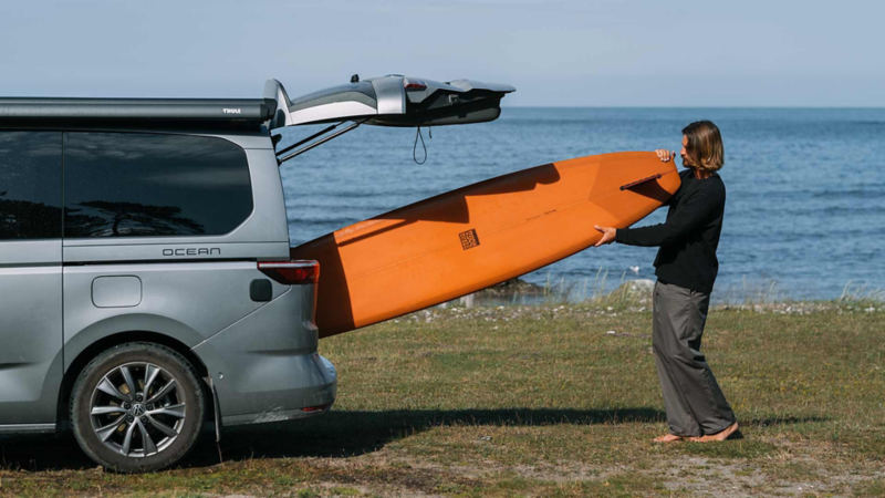 Sebastian skjuter in surfbrädan bak i VW California husbil.