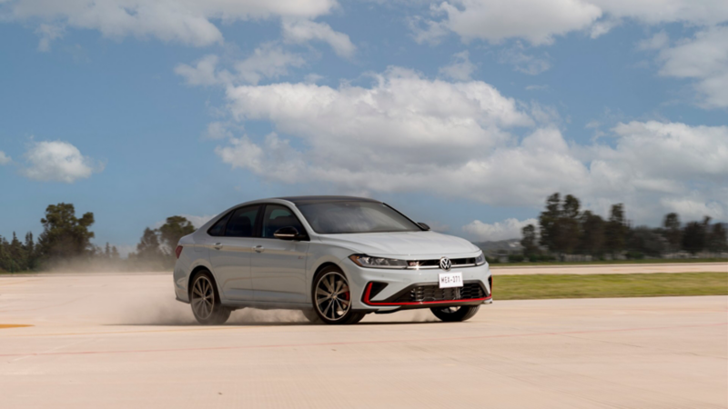 Jetta GLI 2026 blanco en movimiento sobre pista. Sedán deportivo de Volkswagen levanta polvo.