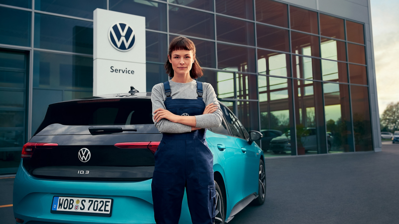 Une collaboratrice du service entretien VW se tient devant une VW ID.3.