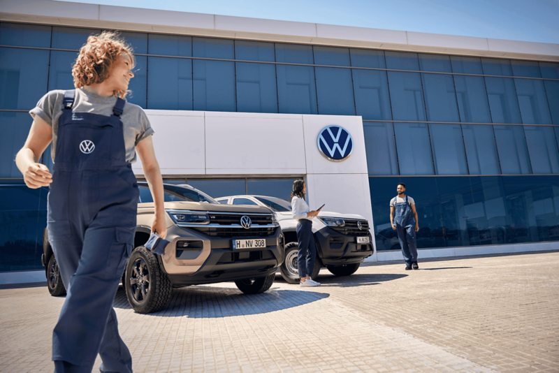 Pracownicy serwisu stoją obok dwóch Volkswagenów Amarok zaparkowanych przed salonem.