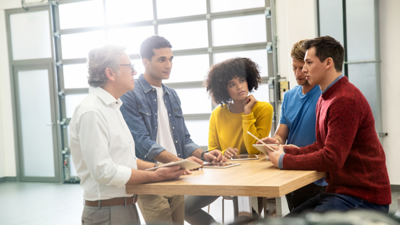 Five business professionals in conversation at a table