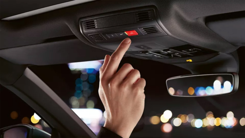 Une personne appuyant sur le bouton d'urgence rouge SOS au plafond d'une voiture.