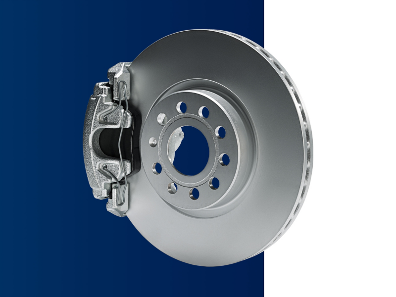 A VW technician knelt next to an exposed brake disc and pad