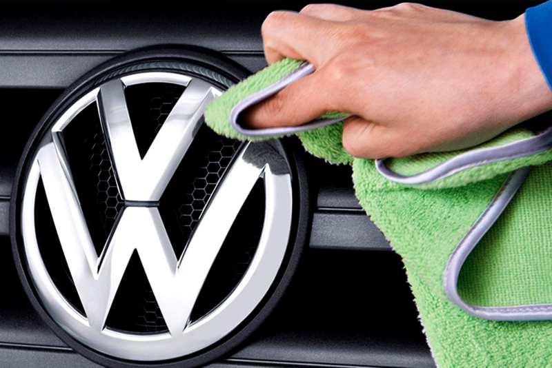 A VW service employee cleaning off a VW vehicle badge.