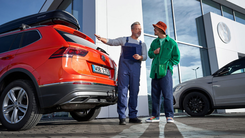A Volkswagen mechanic showing a customer around the outside of his serviced Tiguan outside of a Volkswagen service centre