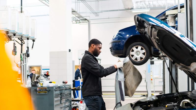 A technician standing over an open bonnet of a VW holding a car cover