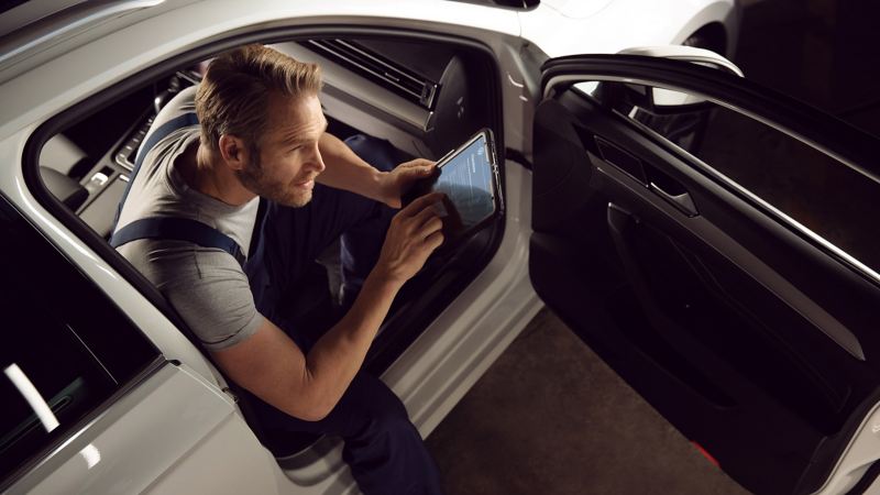 VW mechanic holding an iPad sat in the front of a VW car
