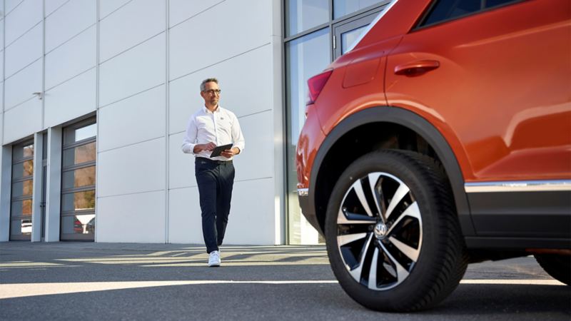 Un homme, tablette en main, se dirige vers une Volkswagen rouge.