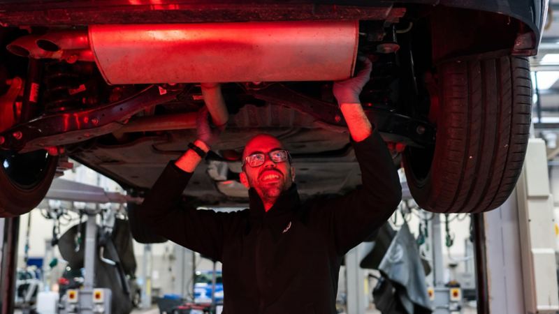 A VW technician inspecting under the chassis of a car