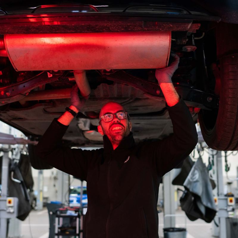 A VW technician inspecting under the chassis of a car