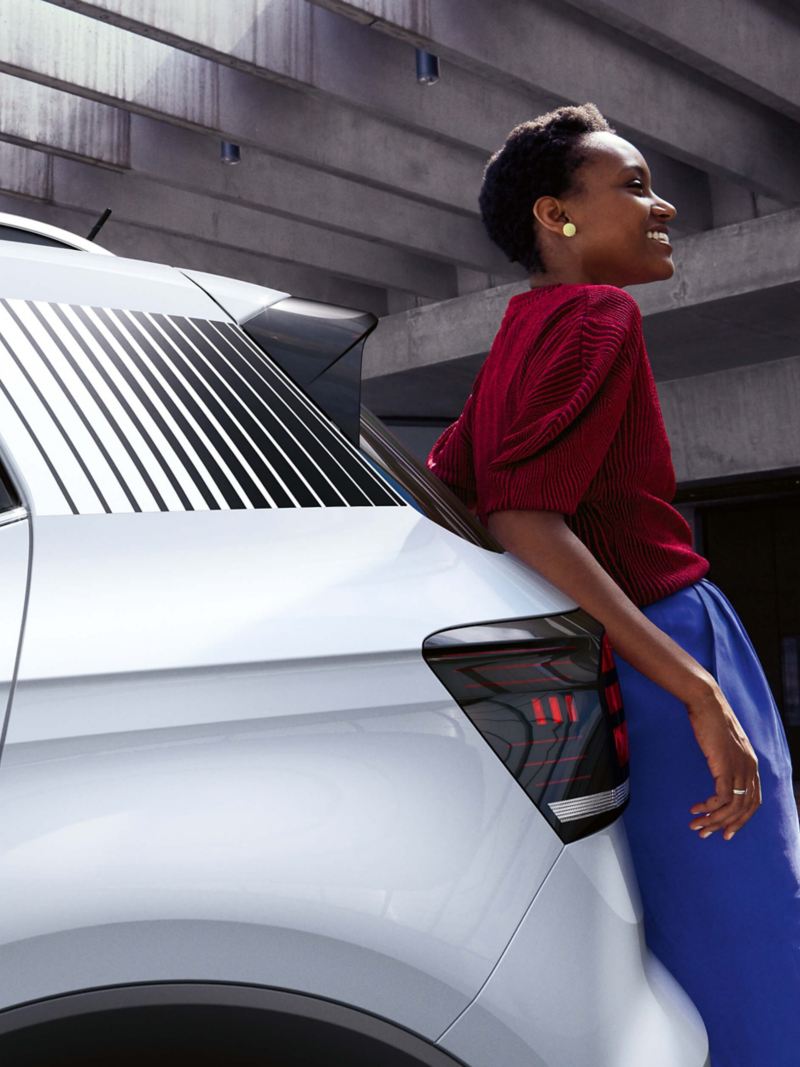 A woman leaning on the back of a Volkswagen vehicle