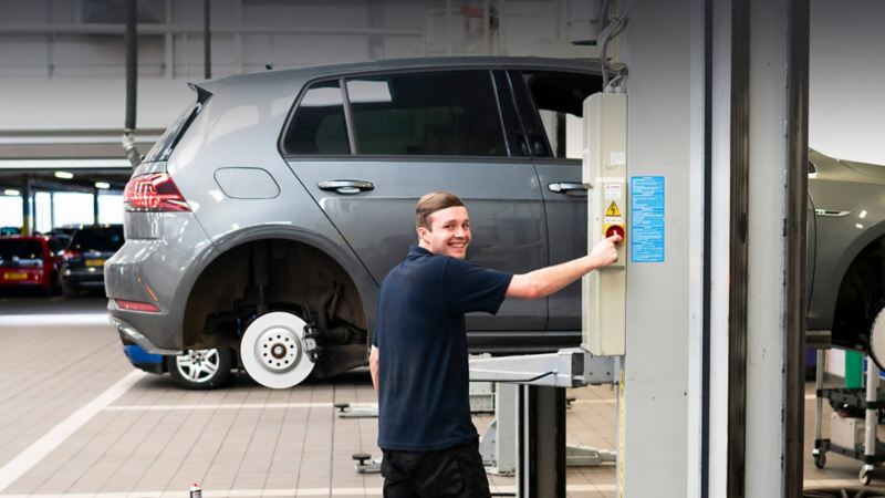 A technician working on a VW Golf that's raised on a ramp with the wheel removed