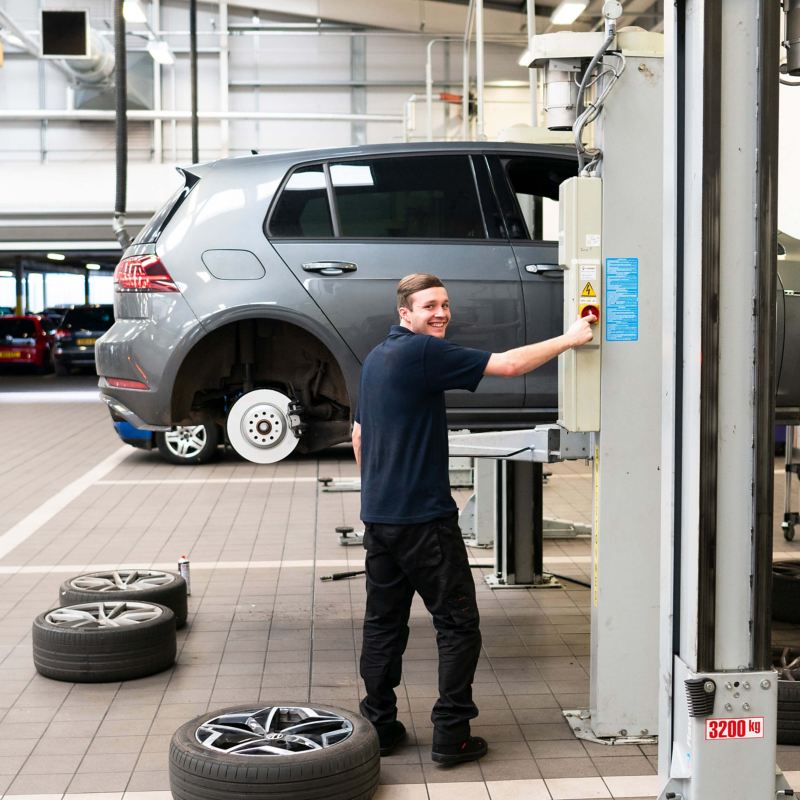 A technician working on a VW golf that's raised on a ramp with the wheel removed